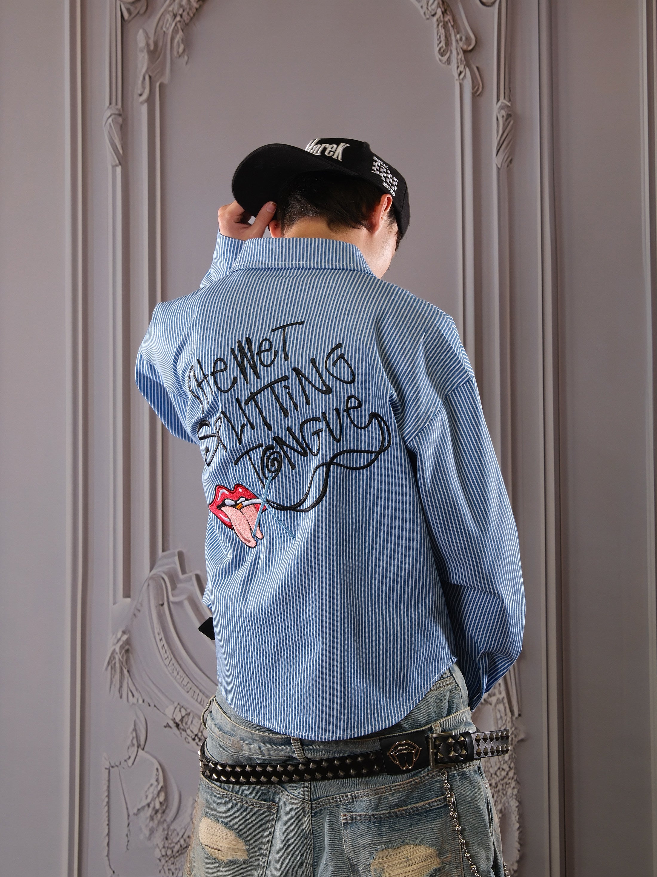 Person wearing a blue shirt with text and graphics, standing against an ornate wall.