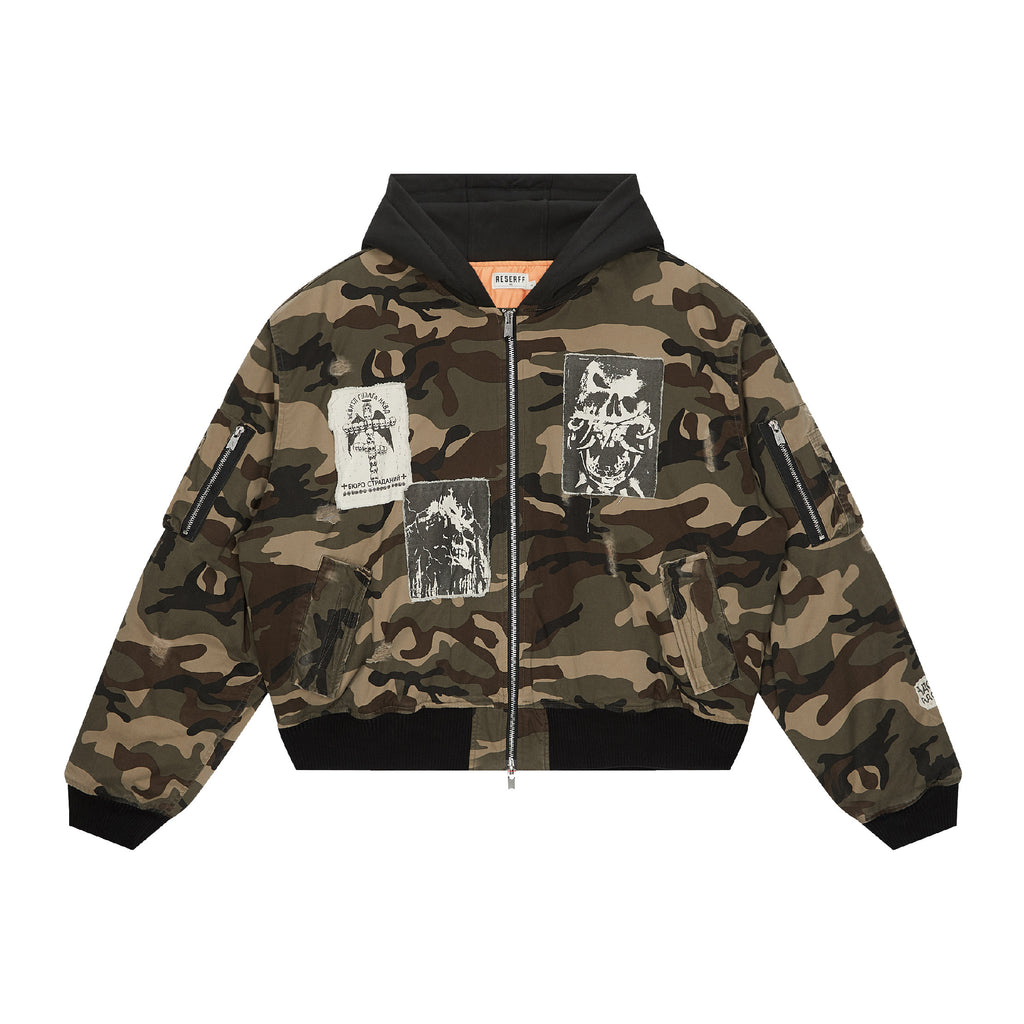 A camouflage hooded bomber jacket with black ribbed trim, a front zipper, and multiple graphic patches on the front and sleeves, shown against a plain white background.