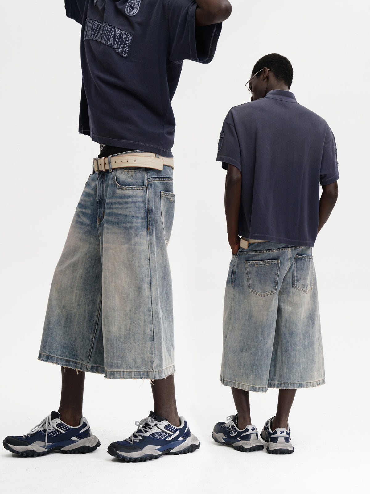 Two people wearing denim skirts with a plain background