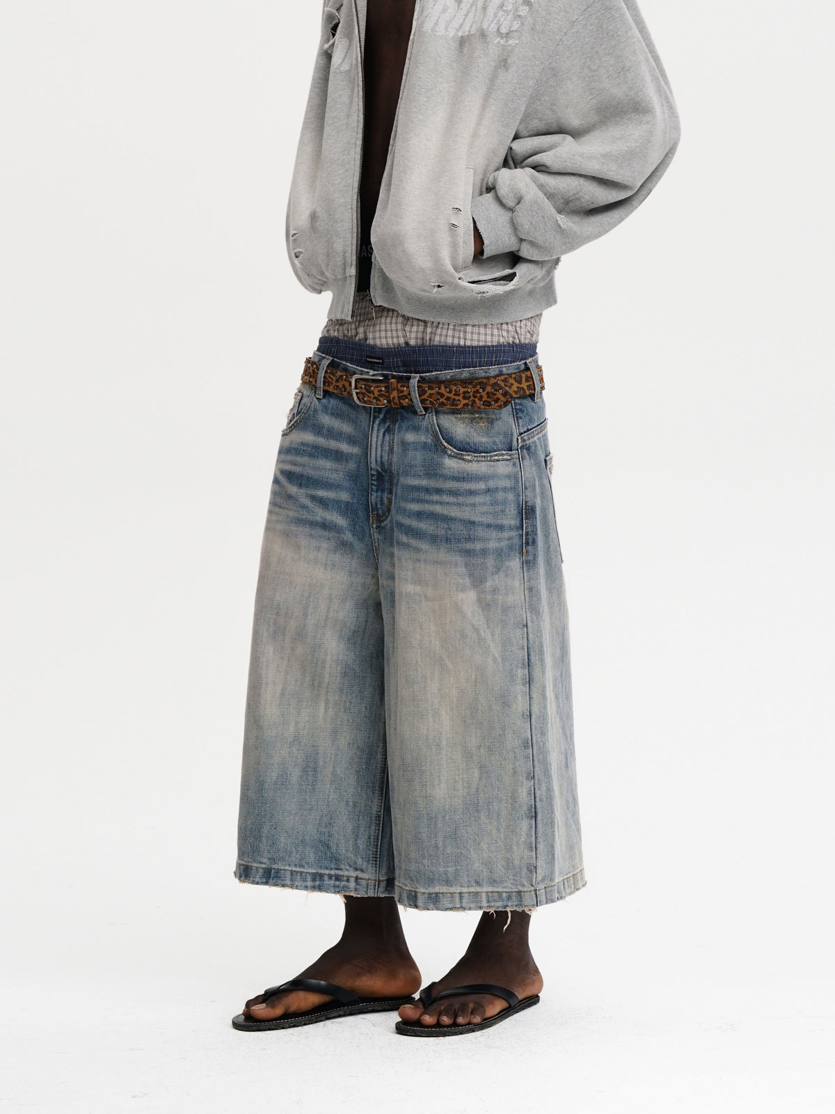 Person wearing a light gray sweatshirt, patterned shirt, and wide-leg blue jeans on a white background